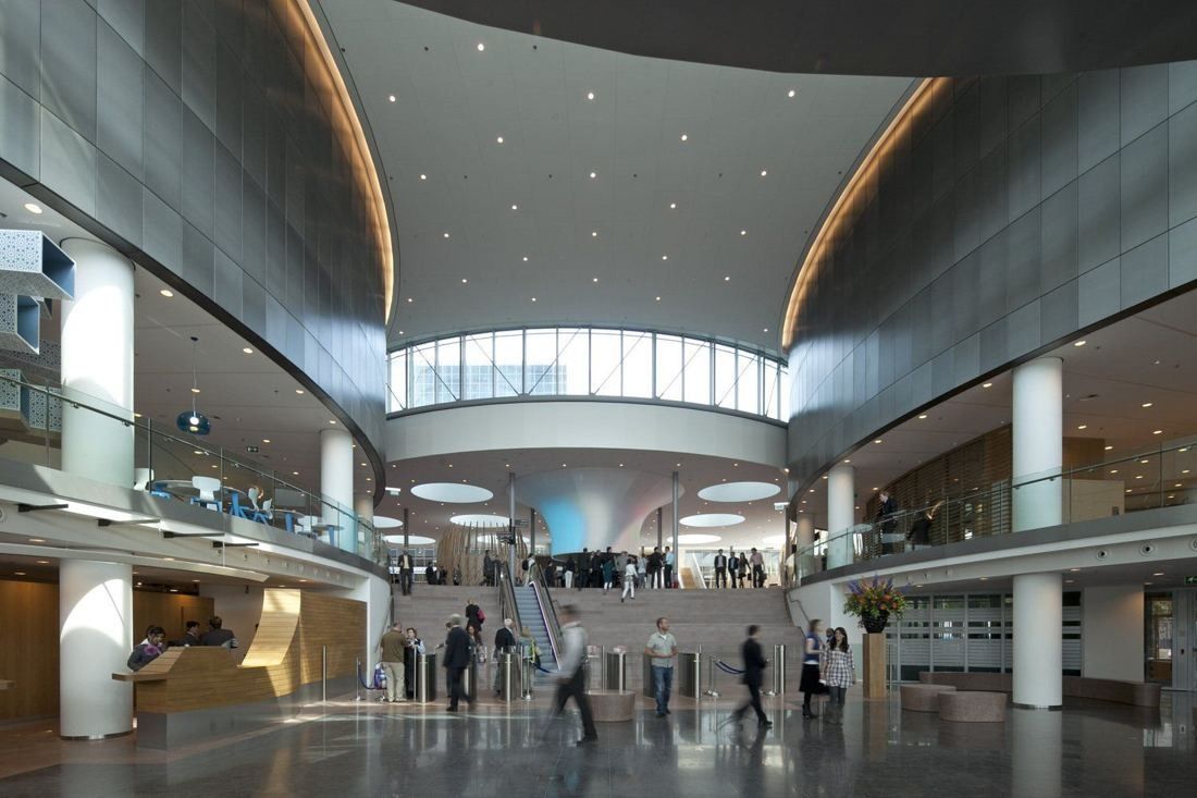 Rabobank: Large curved atrium with grey wall panels, a wide stair with escalator and turnstiles, and a clerestory window at the top