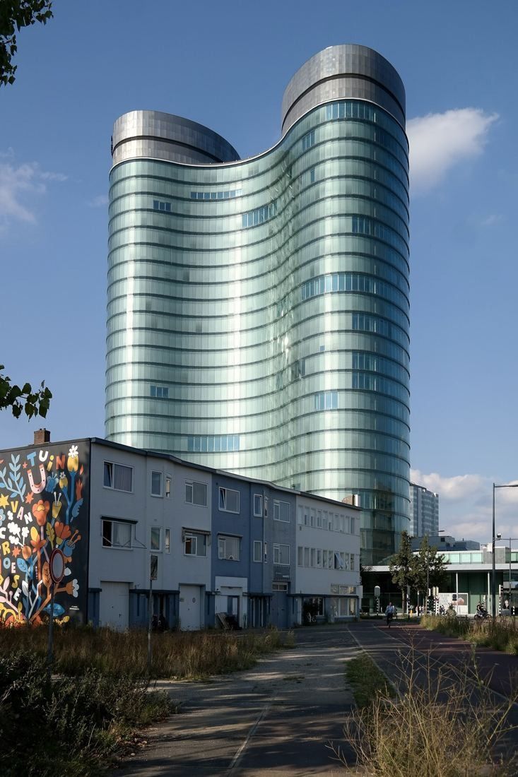 Rabobank: The glass towers behind a low building with a large mural, under a partly cloudy sky