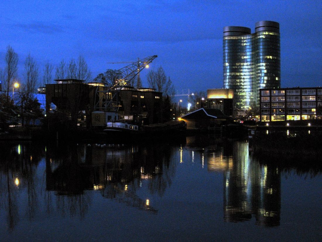 Rabobank: The lit towers reflected in still water at blue hour, with a harbour crane in the foreground