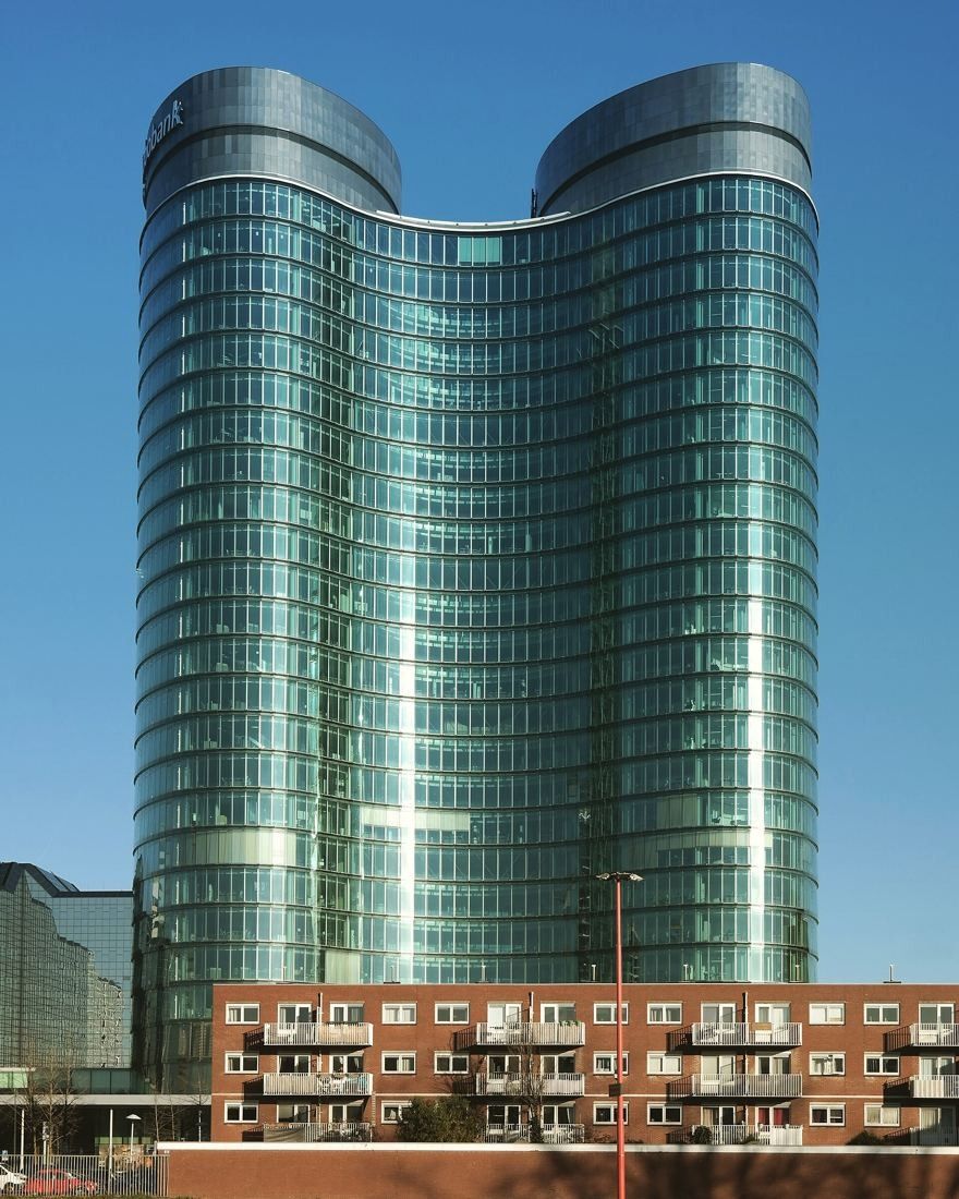 Rabobank: The twin curved glass towers against a clear blue sky above a low apartment block