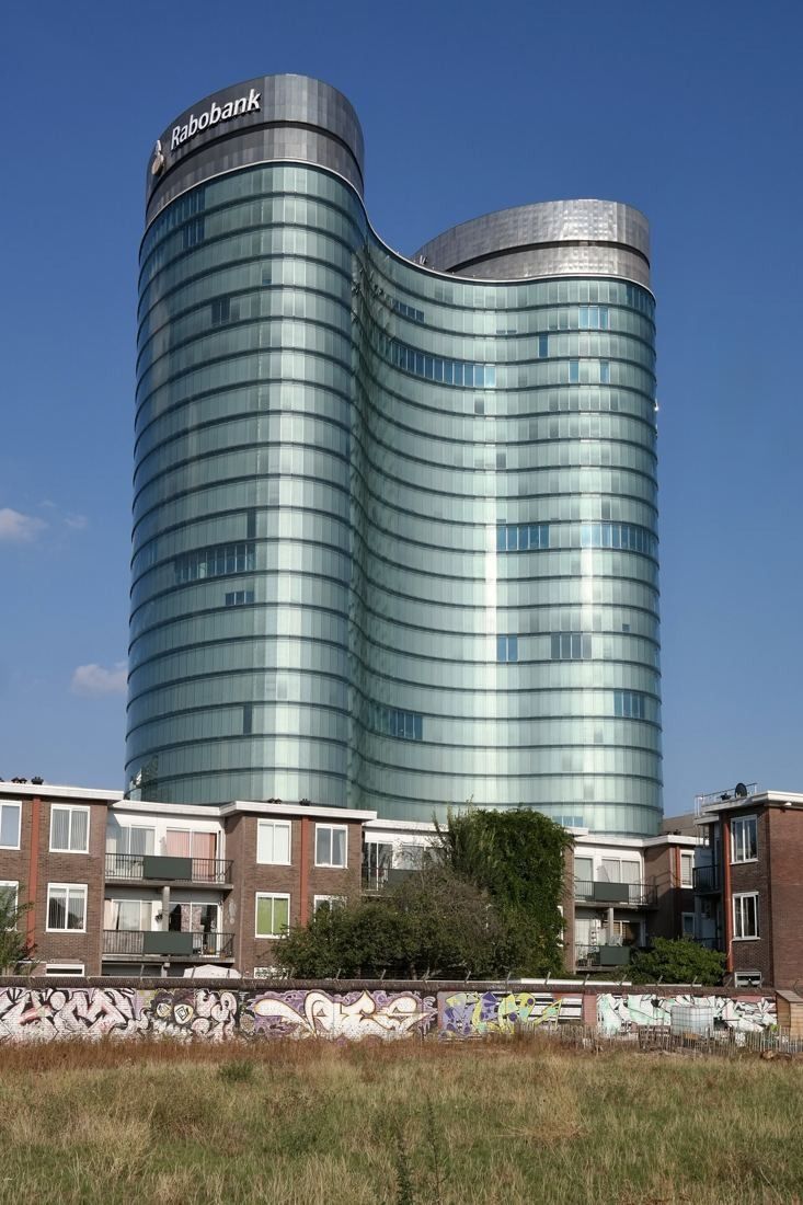 Rabobank: The two curved glass towers seen across a grassy lot above a row of low brick houses