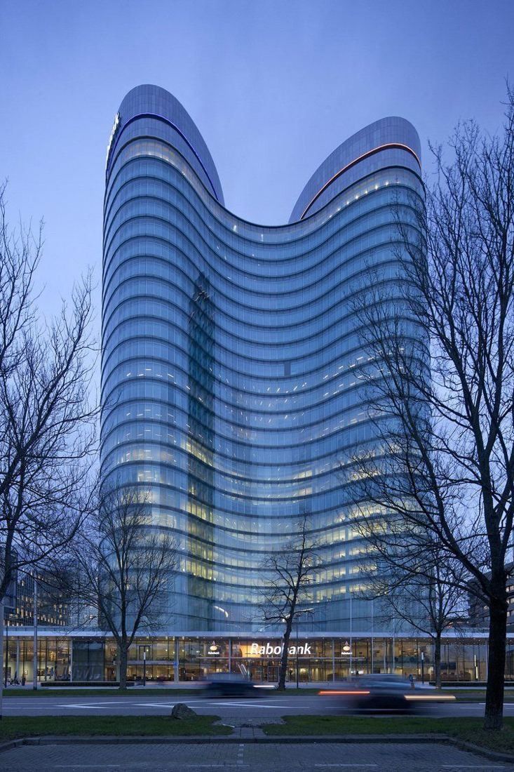 Rabobank: The two curved towers at dusk with lit floors and a road with light trails in front