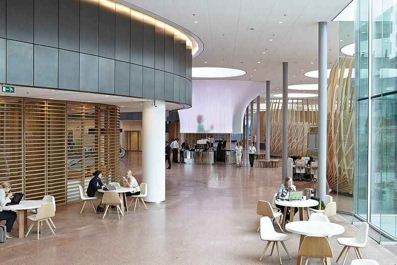 Rabobank: Wide hall with café tables and white chairs, wooden slatted screens, slim columns and a full-height glass facade