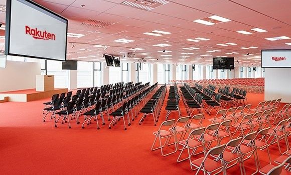 Rakuten Group: Large hall with rows of folding chairs, red carpet and Rakuten screens