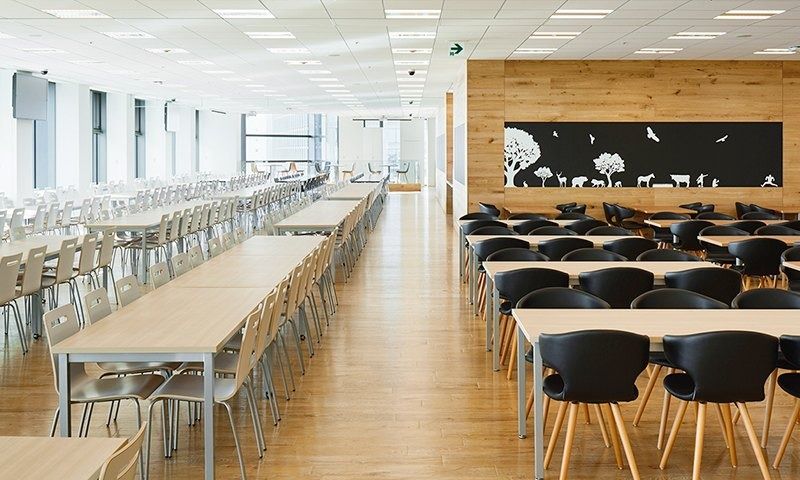 Rakuten Group: Long cafeteria with rows of wooden tables and black chairs