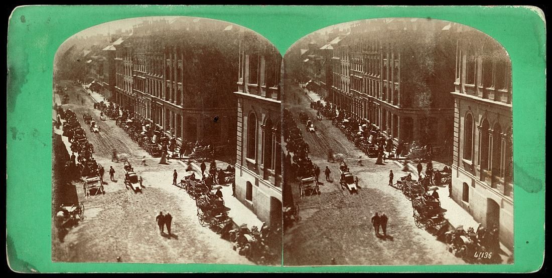Old stereograph of a busy street lined with stone buildings on market day