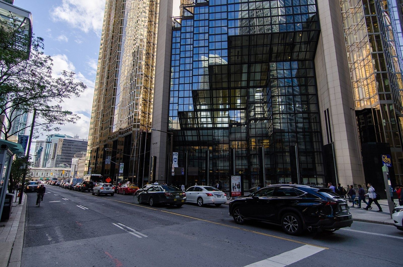 Two gold glass towers joined by a dark glass atrium, seen across a city street with parked cars