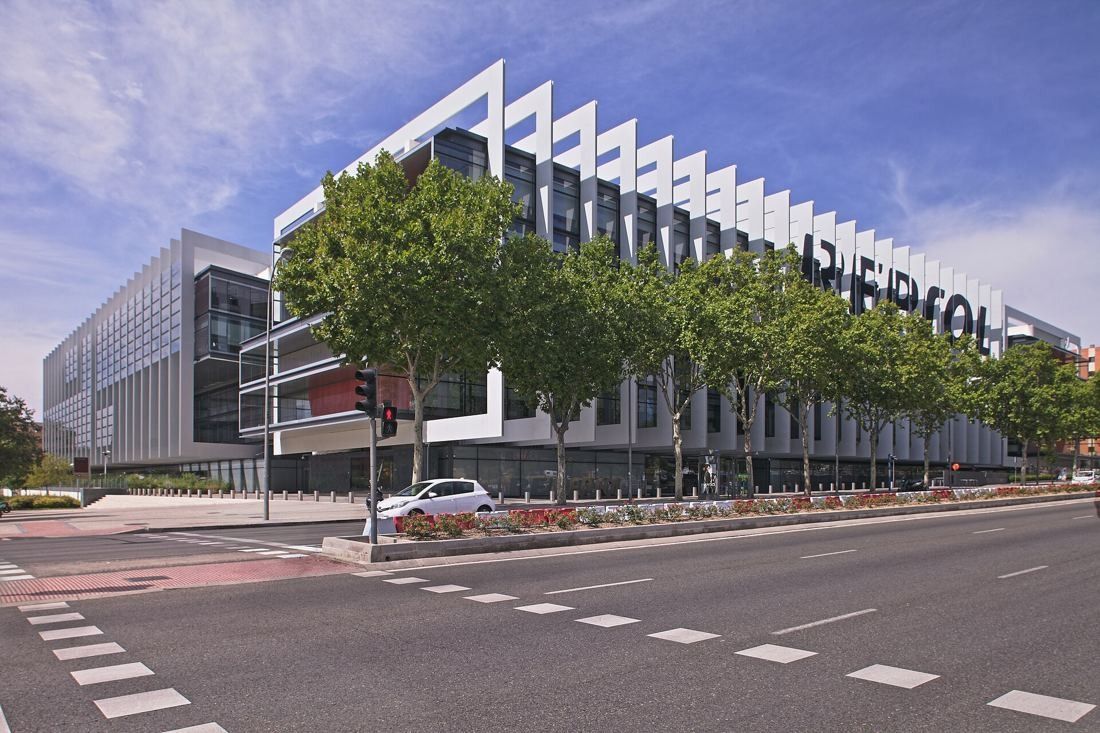 Repsol: Finned façade behind a row of street trees with large lettering along the top