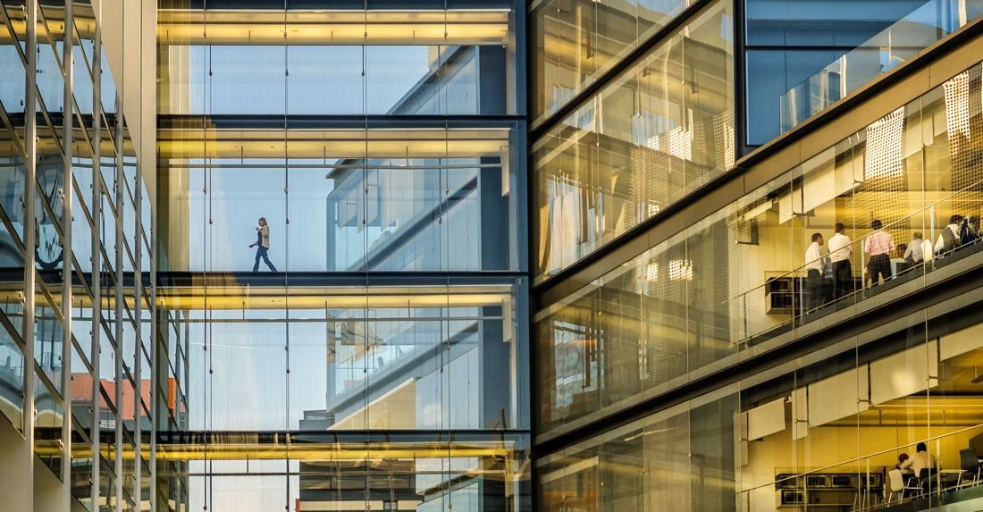 Repsol: Layered glass walls with walkways and offices lit in warm light, a few distant people