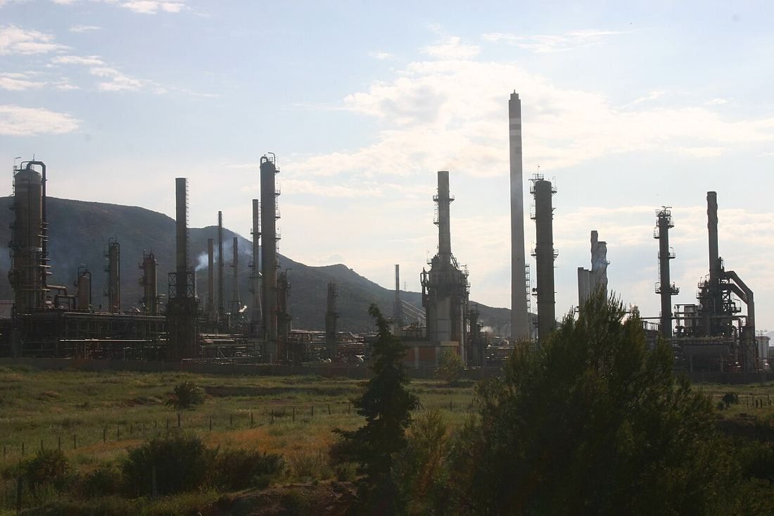 Refinery towers and chimneys below a dry hillside