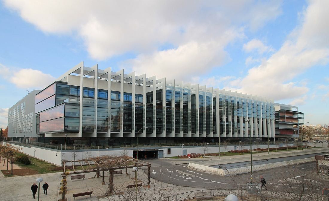 Repsol: Wide view of the finned building above a sunken plaza under a cloudy sky