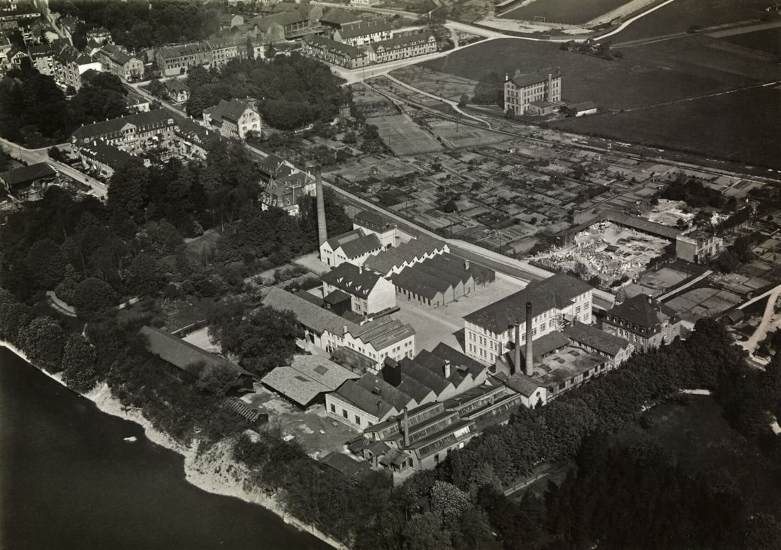 Black-and-white aerial view of a factory complex with chimneys on the bank of the Rhine