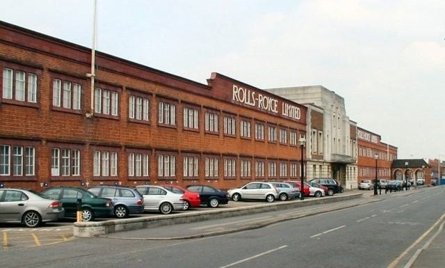 Long red-brick factory frontage with the Rolls-Royce name along a road