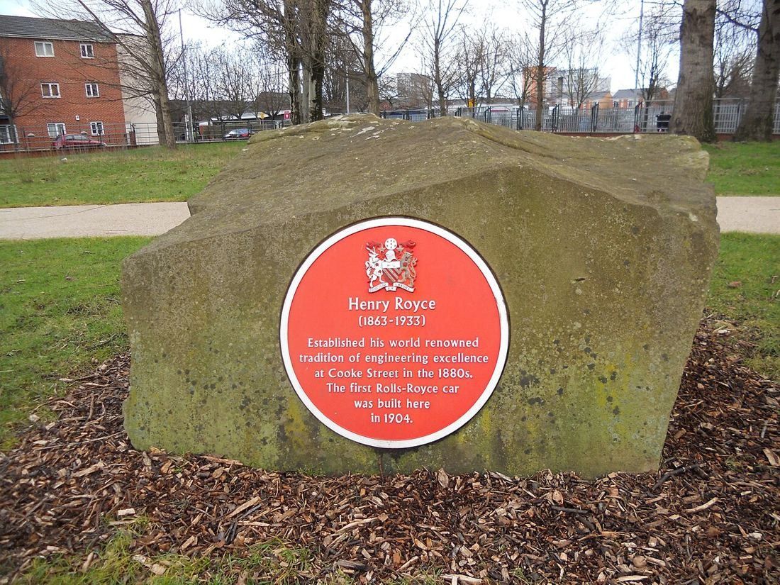 Red commemorative plaque on a boulder in a park marking where Henry Royce built his first car