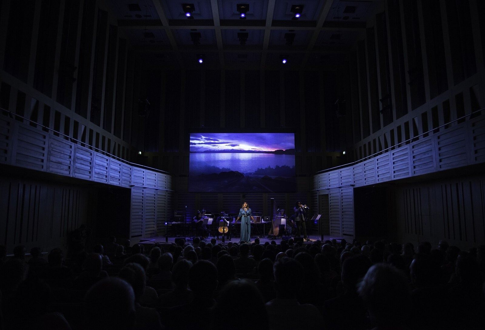 Rolls-Royce: Wood-panelled concert hall seen from the back of a darkened audience, stage lit in the distance