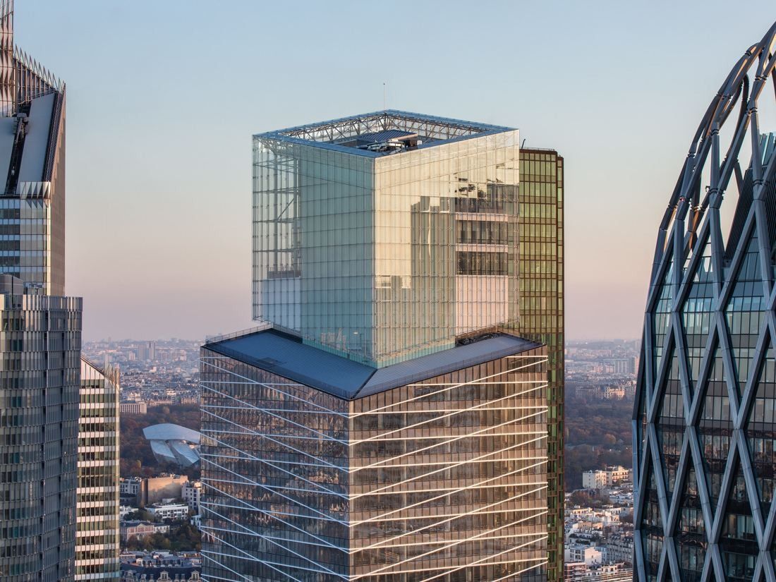 Saint-Gobain: Aerial view of a glass tower top in soft evening light, with the city beyond