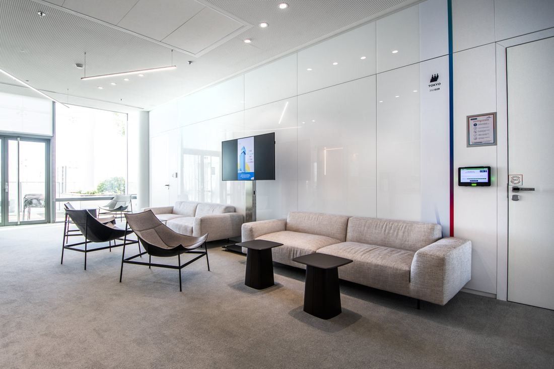 Saint-Gobain: Bright lounge area with white sofas, armchairs and a wall screen