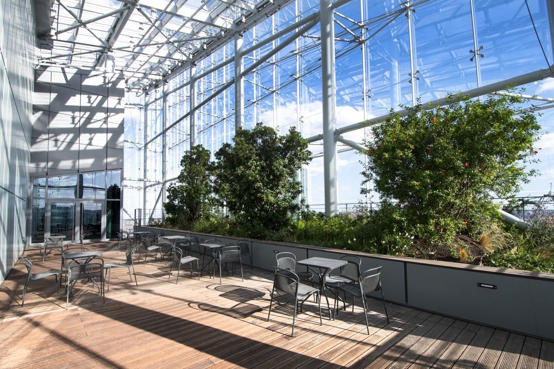 Saint-Gobain: Glass-roofed terrace with trees in planters and metal chairs