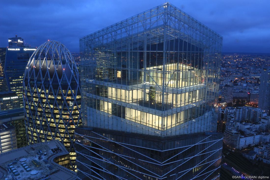 Saint-Gobain: Glass-topped tower lit up at dusk beside an egg-shaped tower and the Paris skyline
