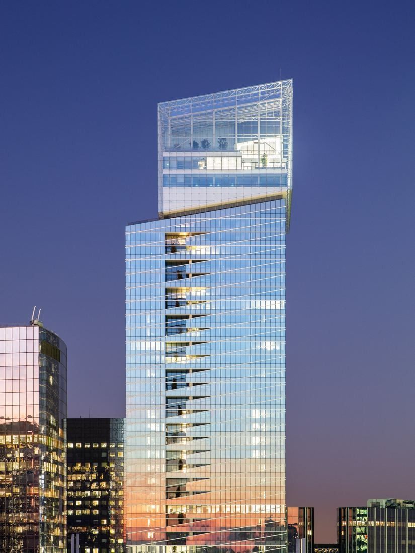 Saint-Gobain: Slender glass tower lit at twilight among lower office buildings