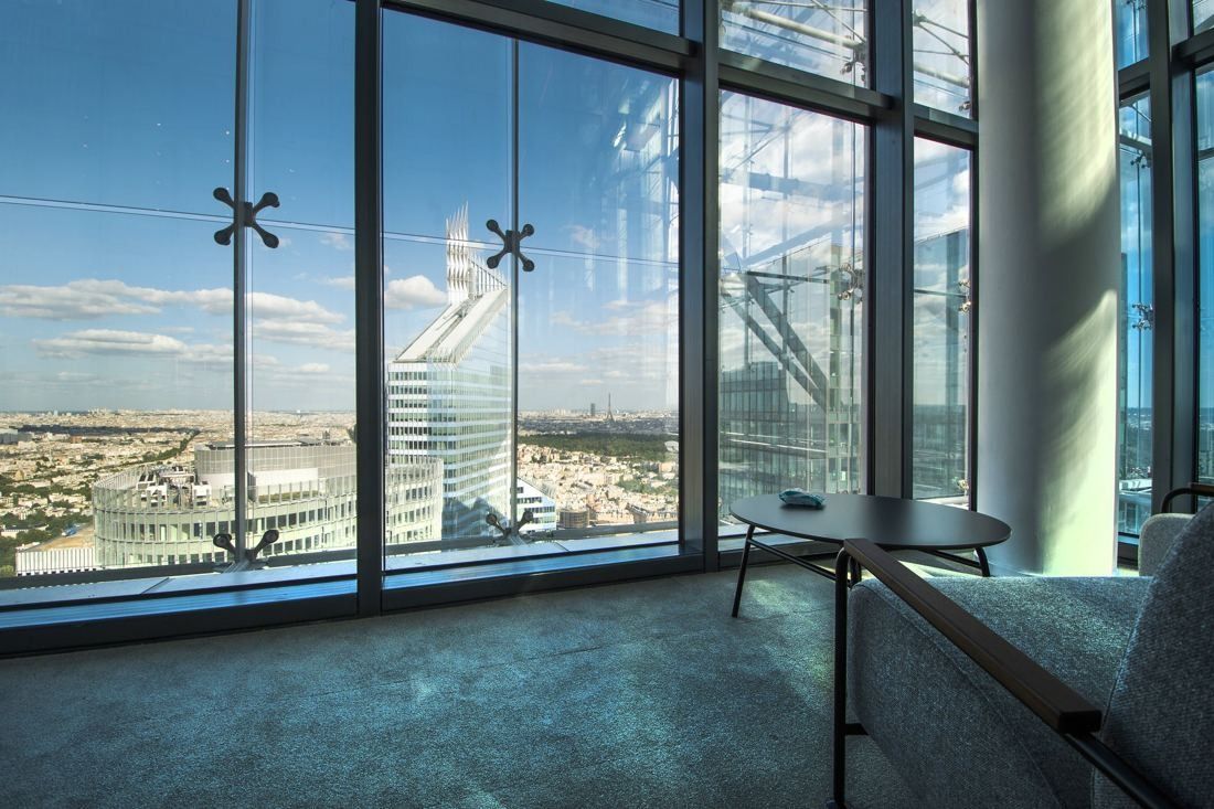 Saint-Gobain: Small table and chairs beside floor-to-ceiling windows looking over Paris