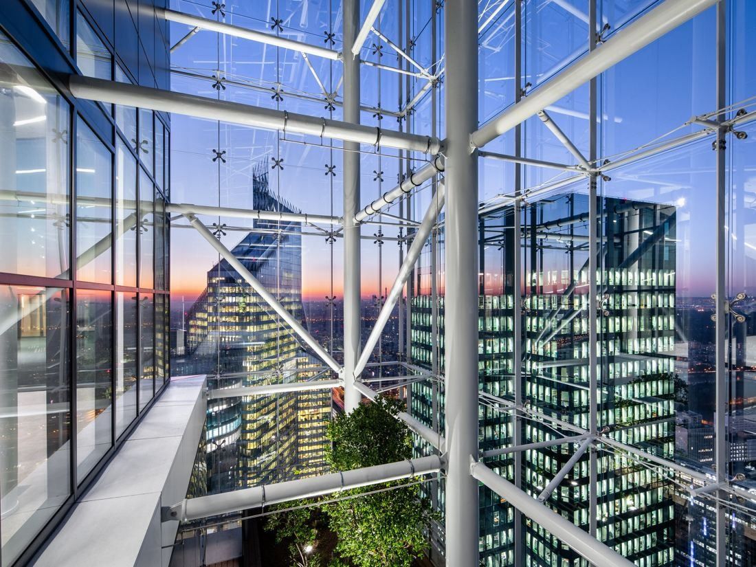 Saint-Gobain: Steel and glass structure inside a double-skin glass crown with planters and a view of towers at sunset