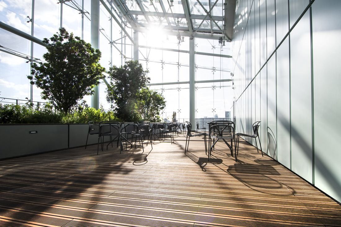 Saint-Gobain: Sunlit glass hall with trees, plants and tables on a wooden floor