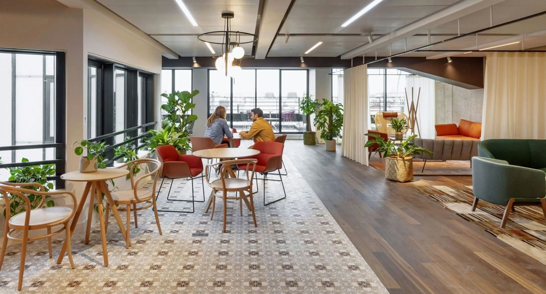 Sanofi: Bright lounge with patterned tile floor, bentwood chairs, plants and curtains, two people seated at the far end