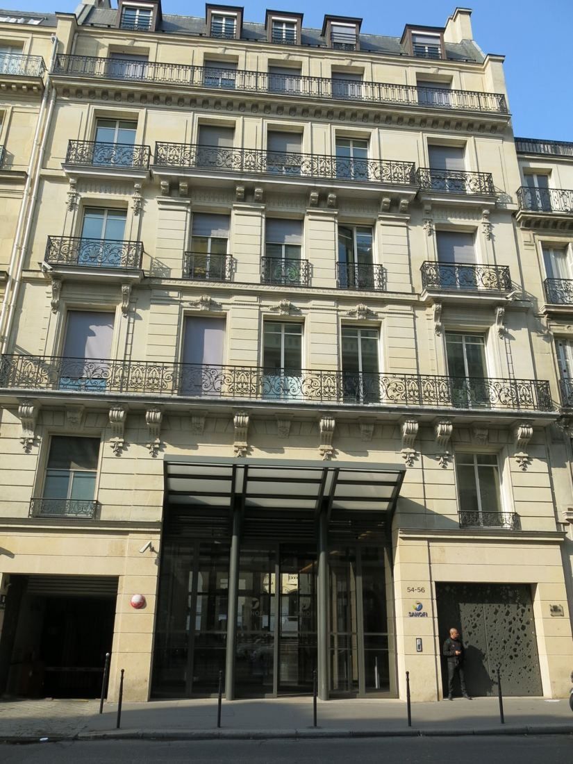 Cream stone Haussmann building with wrought-iron balconies and a glazed ground-floor entrance on a Paris street
