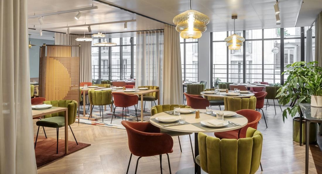 Sanofi: Dining room with round tables, green and rust velvet chairs, glass pendant lamps and tall steel windows