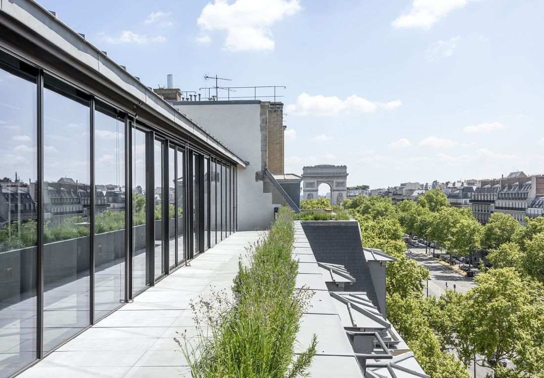 Sanofi: Long rooftop terrace with planted strip beside a glass wall, the Arc de Triomphe in the distance