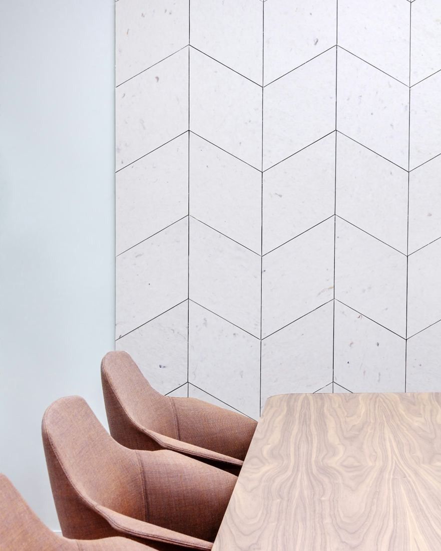 Sanofi: White chevron-pattern acoustic wall panels above pink chairs at a wooden table