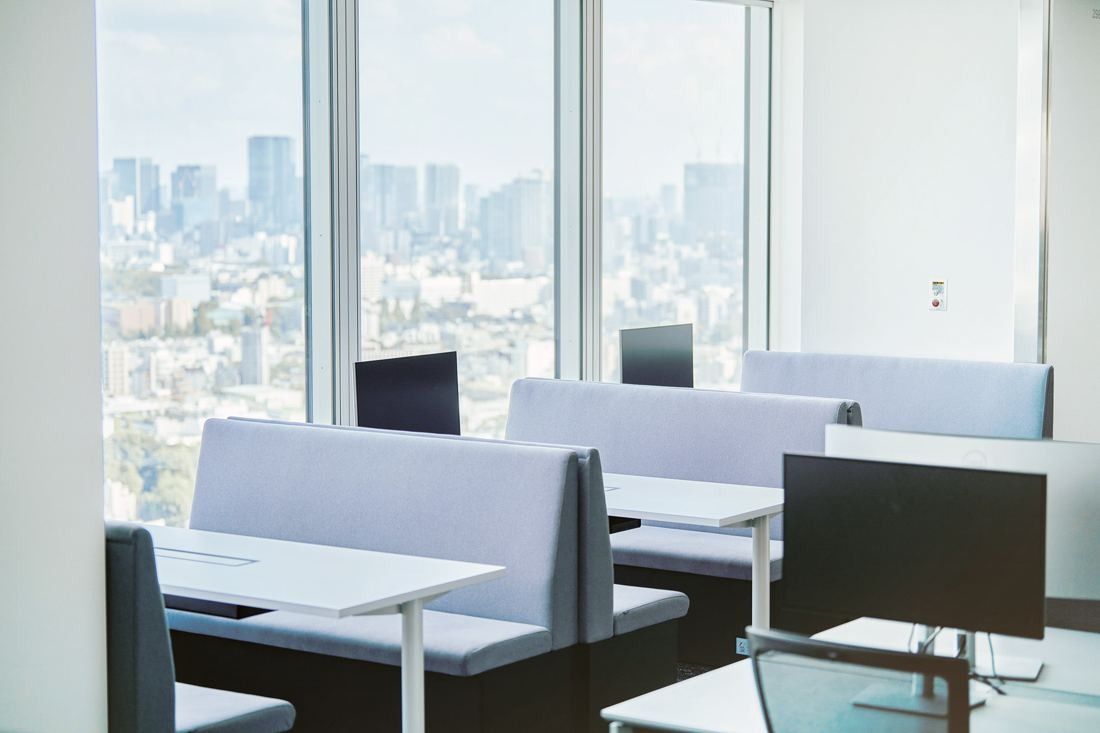 Sansan: Booth seats with high backs and monitors beside tall windows overlooking the city