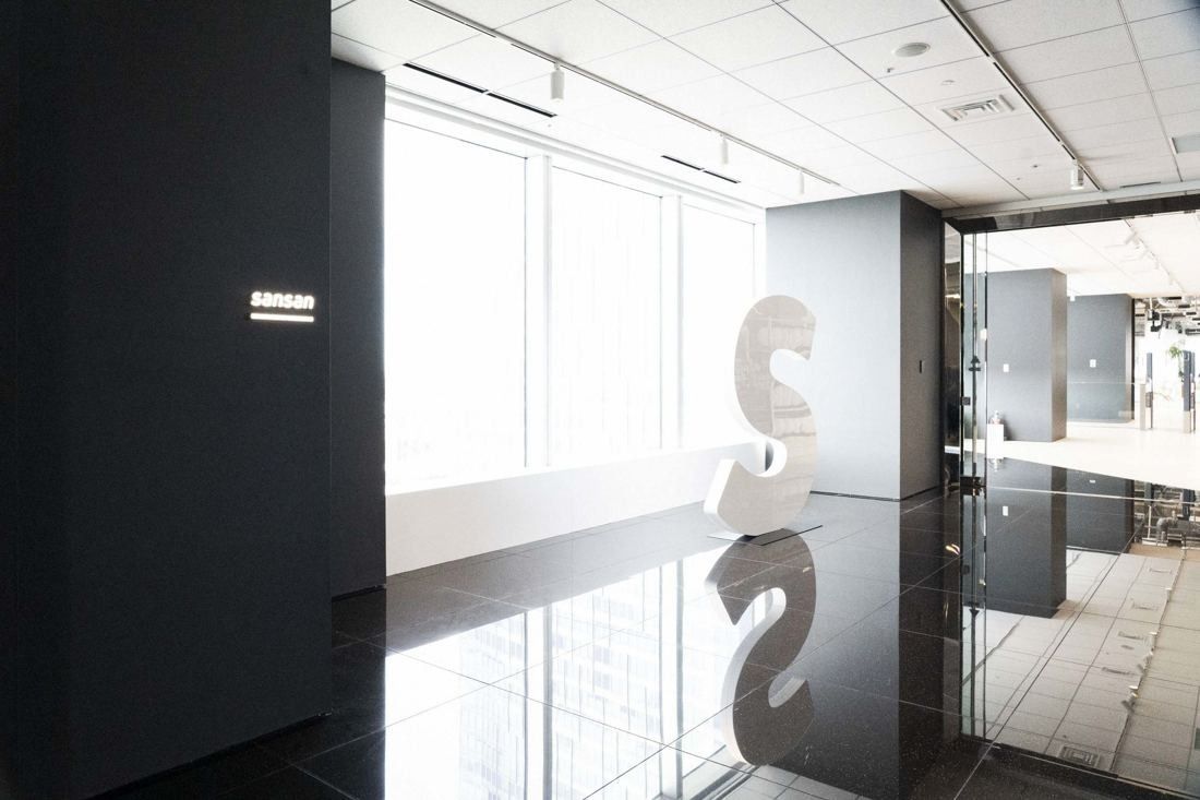 Sansan: Glossy black floor and a large white letter S sculpture by a bright window