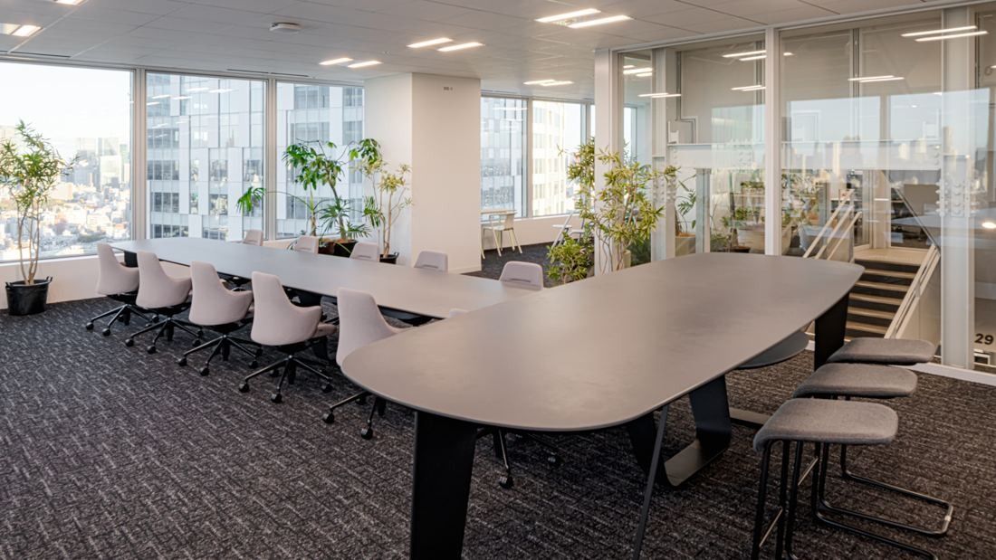 Sansan: Meeting room with a long curved table, white chairs and windows