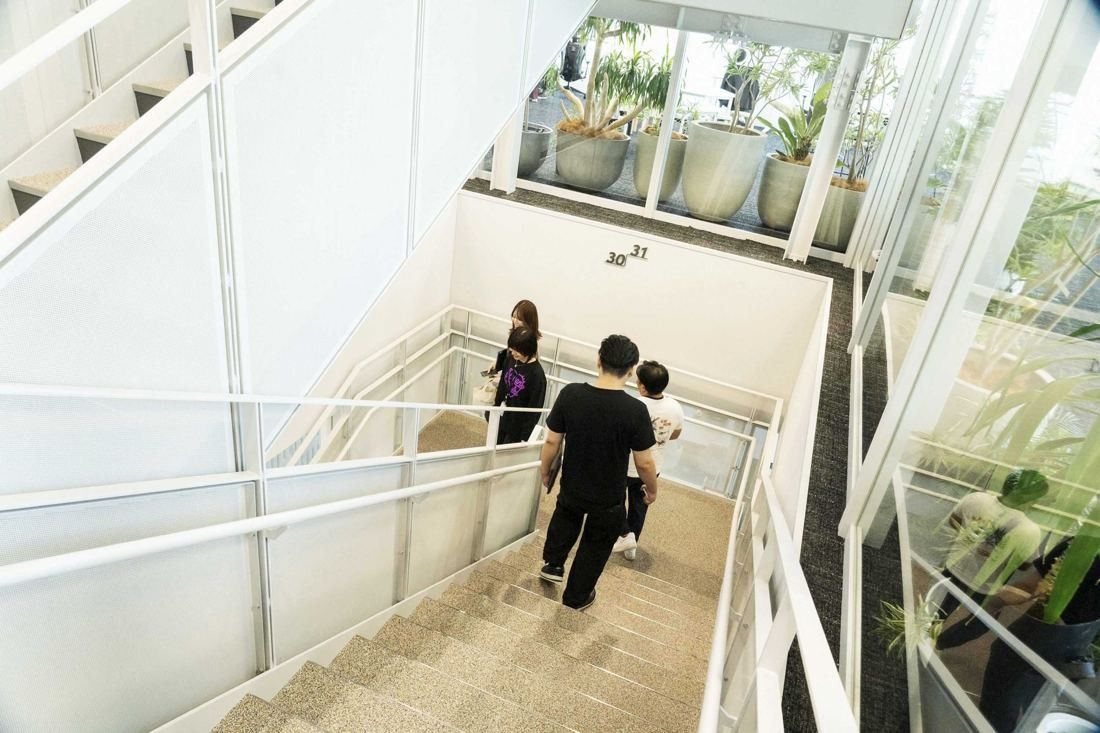 Sansan: People seen from behind walking down a white internal staircase lined with plants