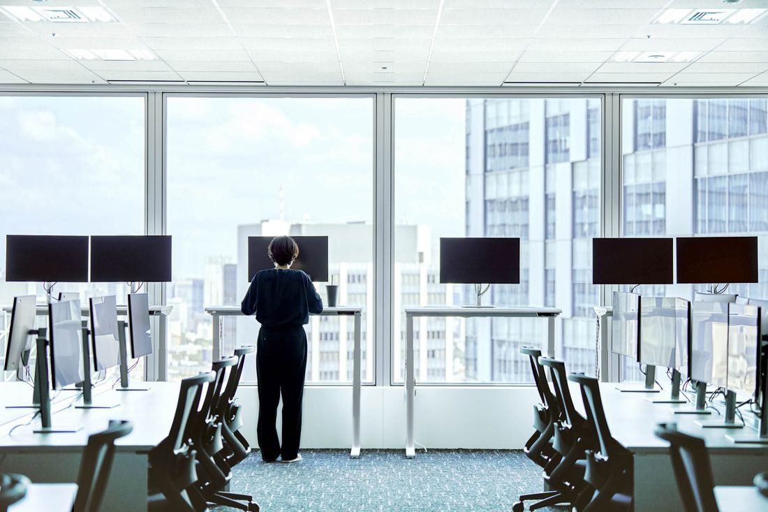 Sansan: Person seen from behind at a standing desk with monitors by the windows