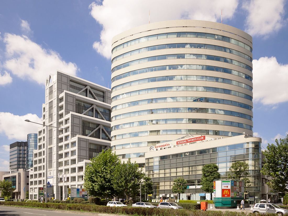 Round glass office tower beside a wide avenue under a blue sky