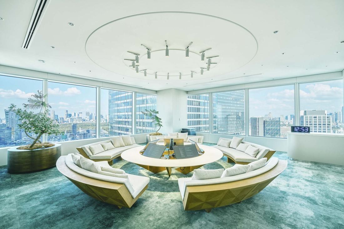 Sansan: Round sunken seating with cushions under a ring-shaped light and wide windows