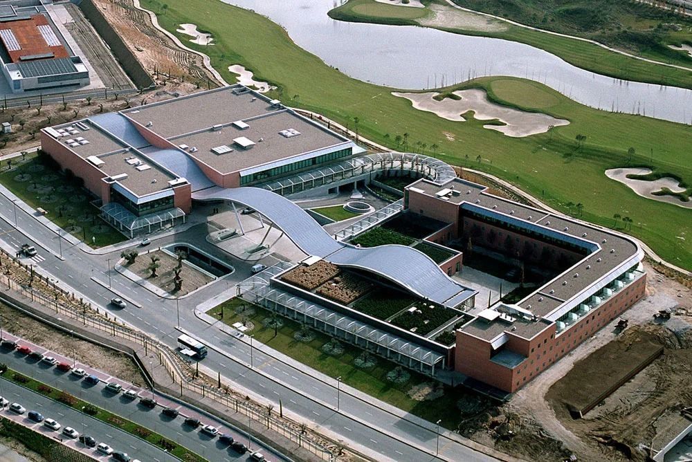 Banco Santander: Aerial view of a building with a curved roof wrapped around a courtyard, beside a golf course