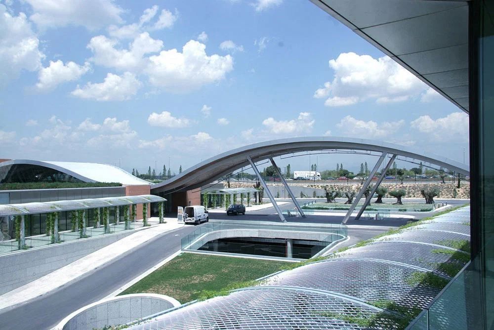 Banco Santander: Curved canopy over a plaza with long glazed buildings and young olive trees
