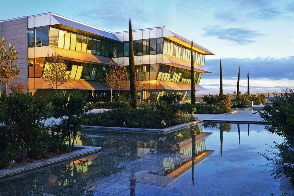 Banco Santander: Glass office building reflected in a still pool at dusk, with cypress trees