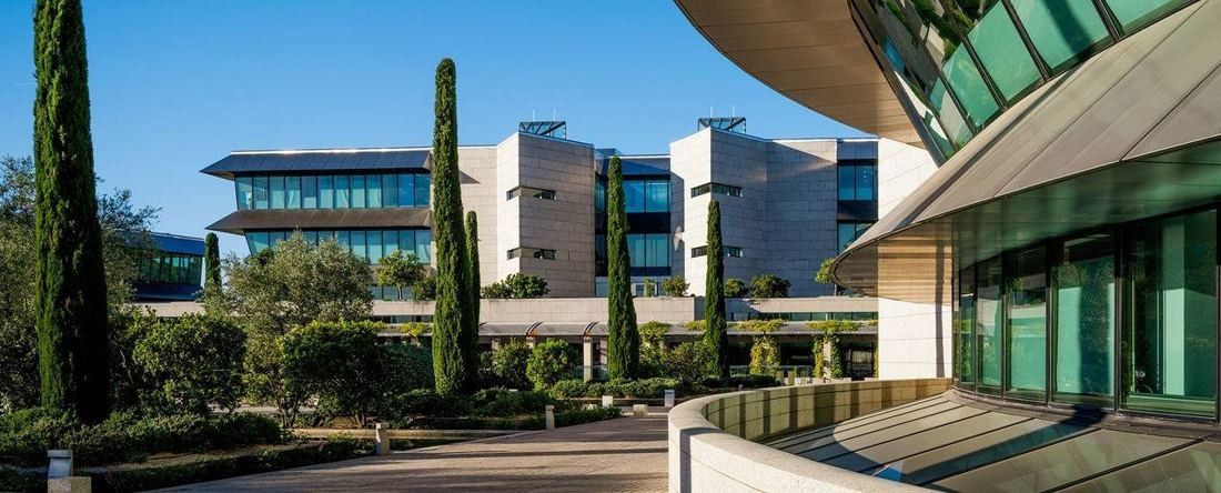 Banco Santander: Glass office buildings seen past a curved facade, with a tree-lined walk