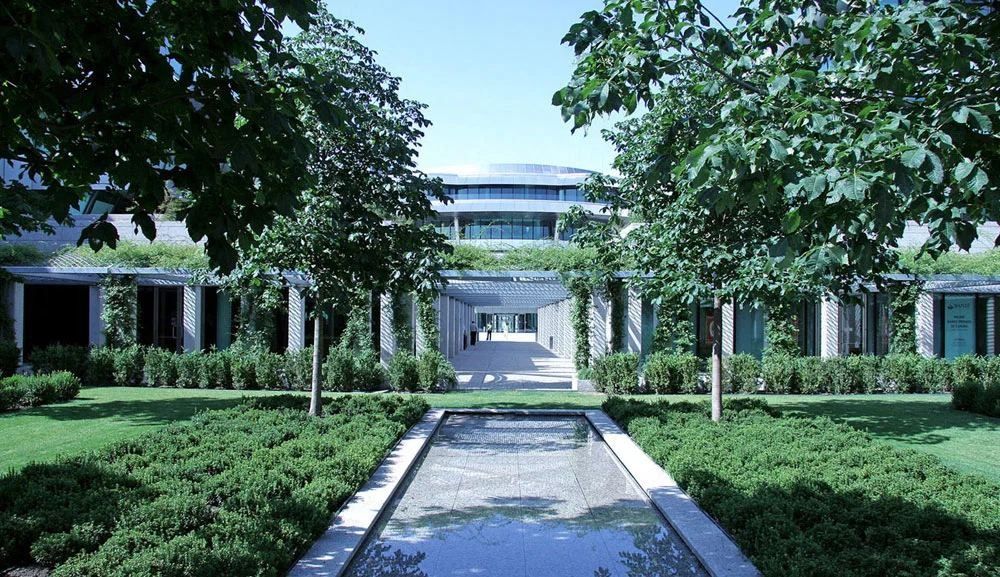 Banco Santander: Long rectangular pool in a lawn courtyard lined with trees, with buildings behind
