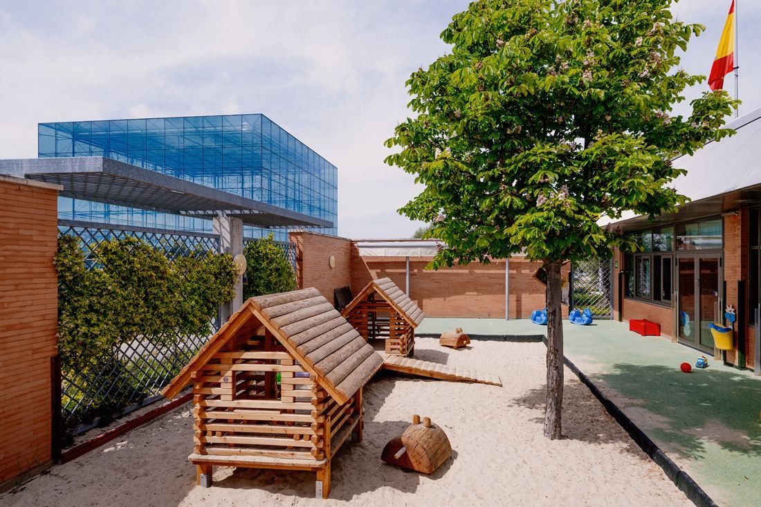 Banco Santander: Nursery playground with small wooden playhouses, sand and a tree