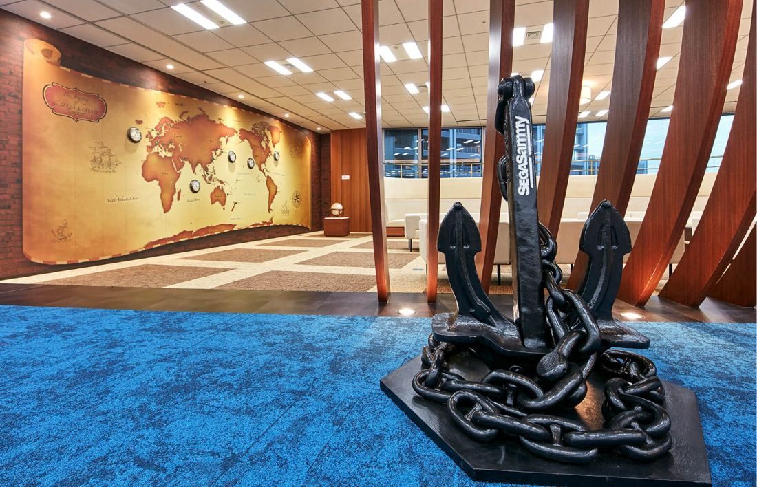 SEGA: Black anchor sculpture with chain on blue carpet in front of a world map wall