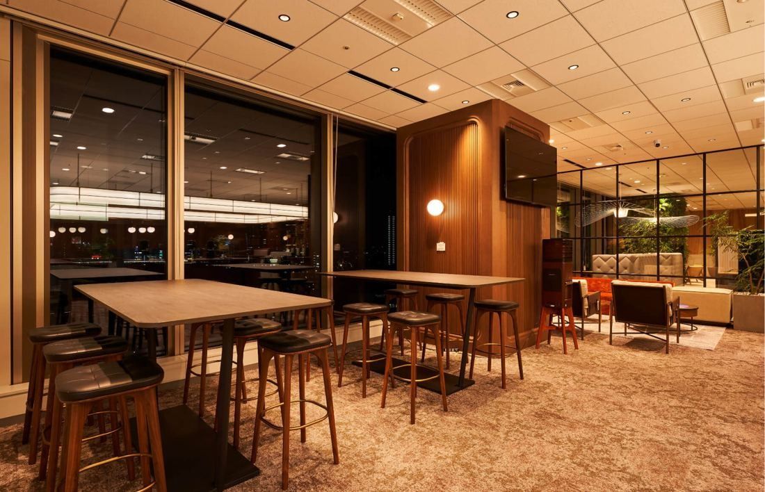 SEGA: Dimly lit lounge with high tables and stools by large windows