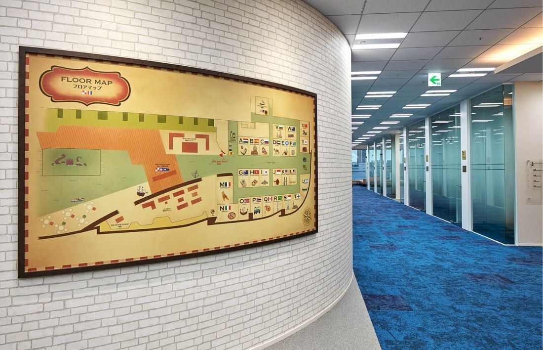 SEGA: Framed floor map on a white brick wall beside a corridor of glass meeting rooms