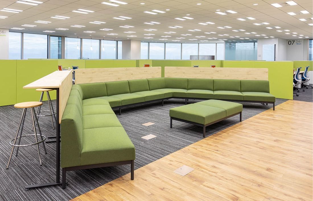 SEGA: Green modular sofa and high counter on a wood-floored area of an open office