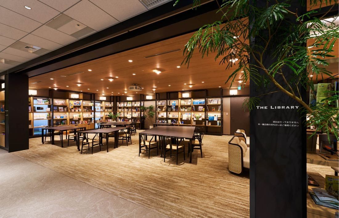 SEGA: Library space with tall bookshelves, tables and a plant at the entrance